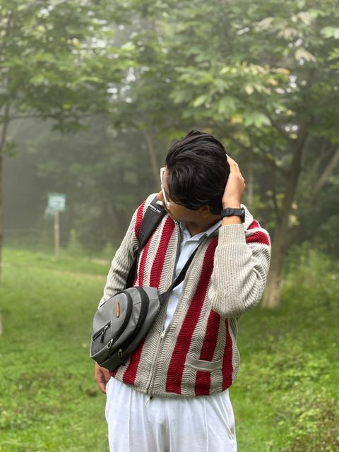 Moaaz Ali in a striped knit cardigan in a misty forest